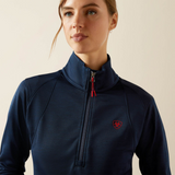 Woman wearing a navy blue pullover with a red logo on a beige background