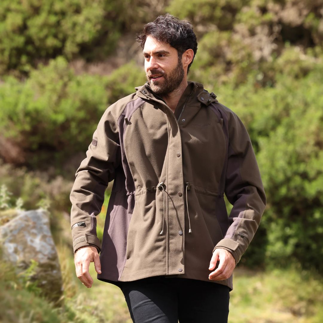 Man wearing a brown jacket outdoors with greenery in the background