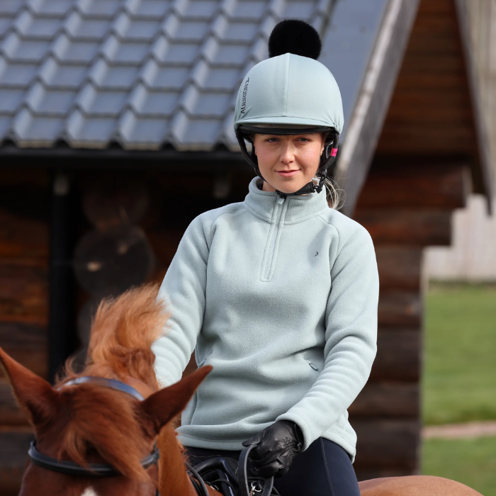 Person in equestrian gear sitting on a horse with a wooden stable in the background