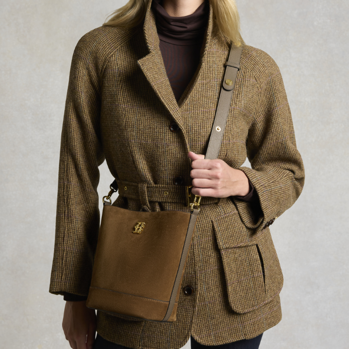 Holland Cooper Country Crossbody Bag Variant Colour Linchen Suede.
A woman wearing a brown and beige houndstooth blazer with a matching belt, carrying a brown suede crossbody bag with a leather strap.