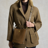 Holland Cooper Country Crossbody Bag Variant Colour Linchen Suede.
A woman wearing a brown and beige houndstooth blazer with a matching belt, carrying a brown suede crossbody bag with a leather strap.