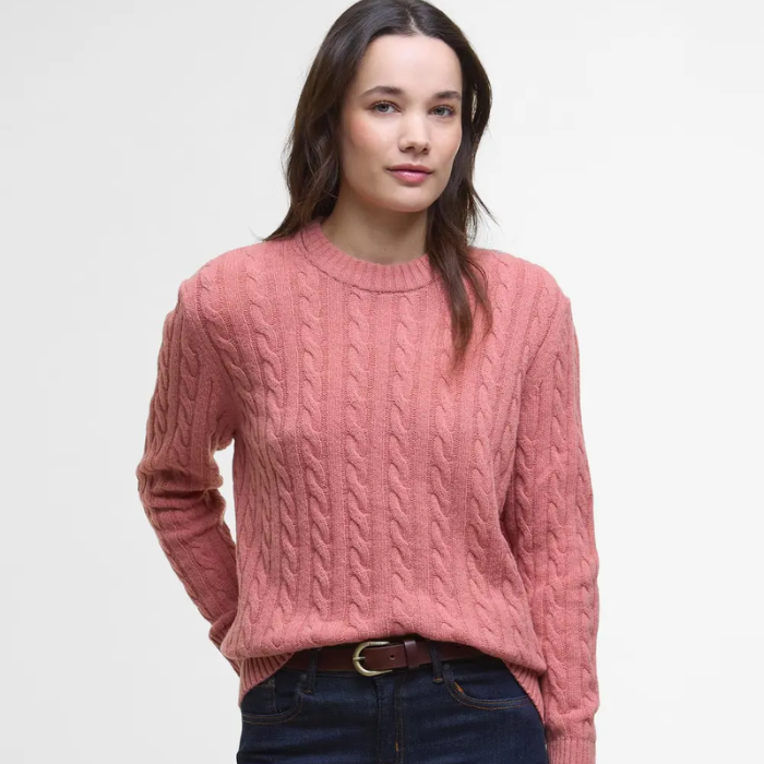 Woman wearing a pink cable knit jumper on a light grey background