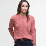 Woman wearing a pink cable knit jumper on a light grey background