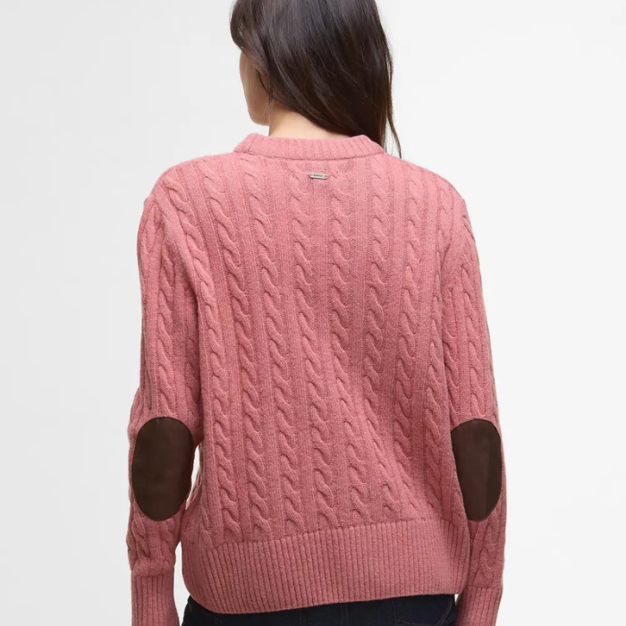 Pink cable knit jumper with elbow patches worn by a person on a light grey background
