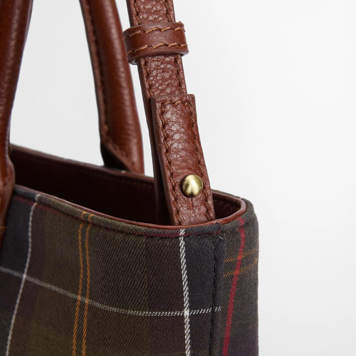 Close up of a tartan bag with brown leather strap on a grey background
