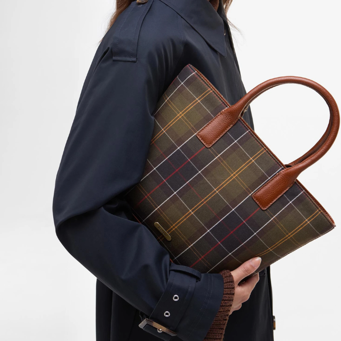 Person holding a tartan bag with brown handles against a white background