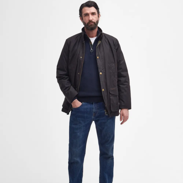Man wearing a dark Barbour jacket and blue jeans on a white background