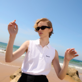 Female on the beach wears the Barbour Ladies Bowford Sleeveless Polo Top in White, styled with a black skirt