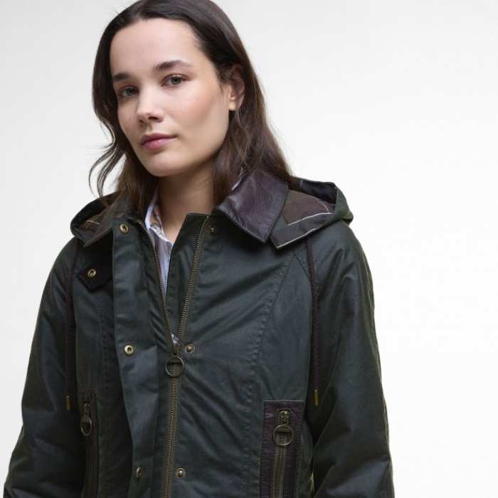 Woman wearing a dark Barbour jacket with a plain background