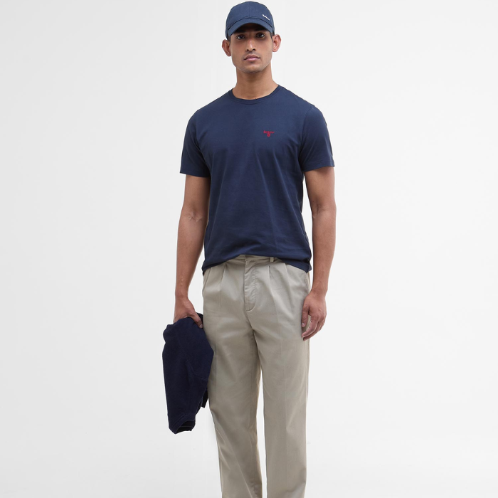 Man wearing a navy t-shirt with a red Barbour logo and beige trousers on a white background