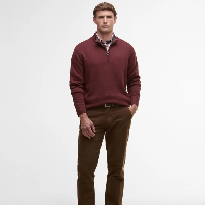 Man wearing a burgundy Barbour sweater and brown pants on a white background