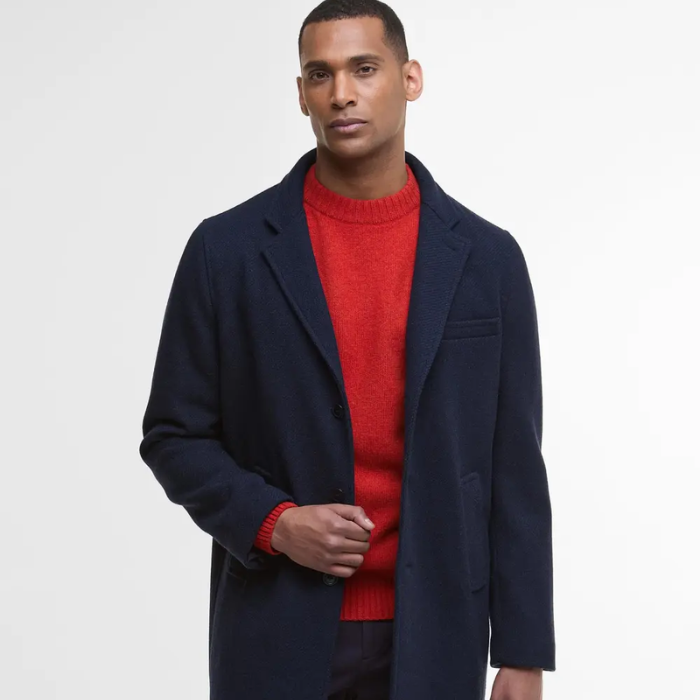 Man wearing a navy wool coat over a red sweater on a white background