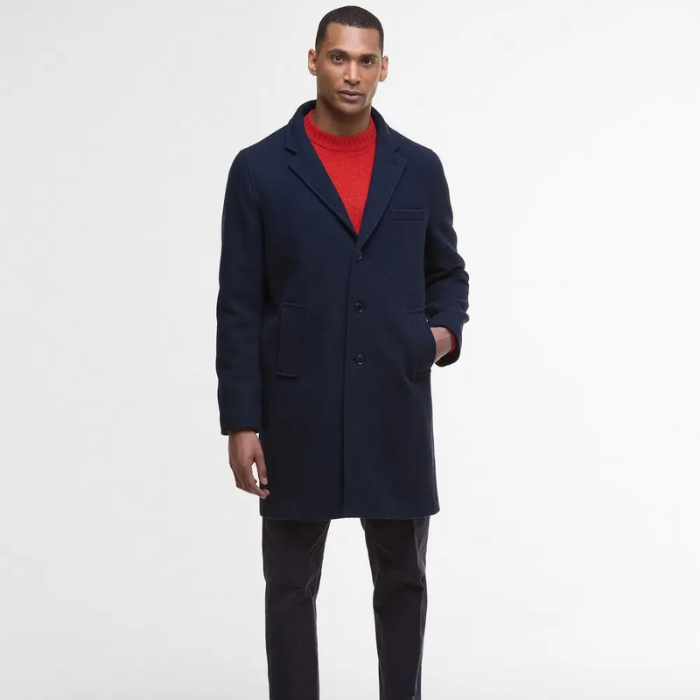 Man wearing a navy wool coat over a red sweater on a white background