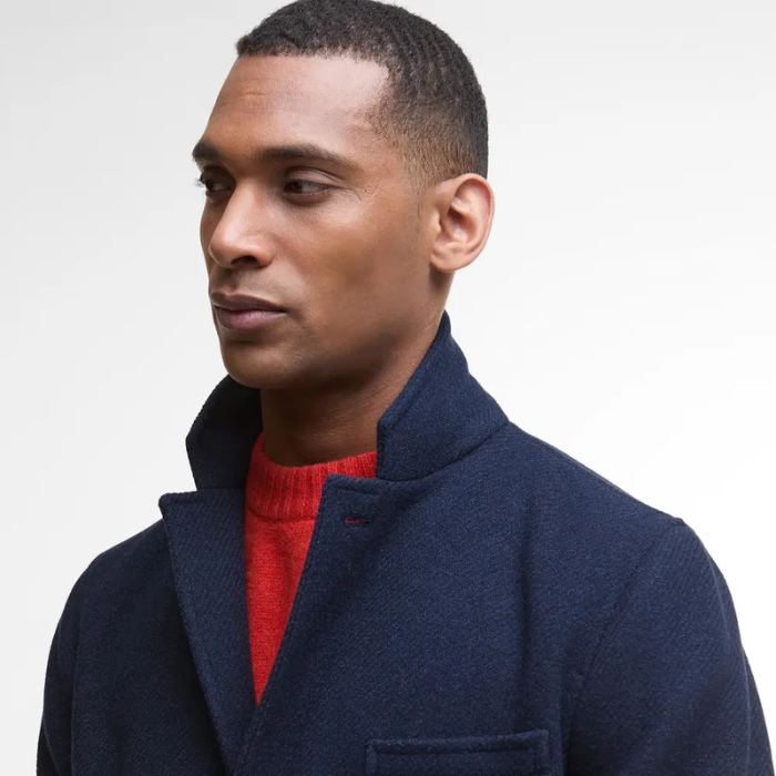 Man wearing a navy wool coat over a red sweater on a light gray background
