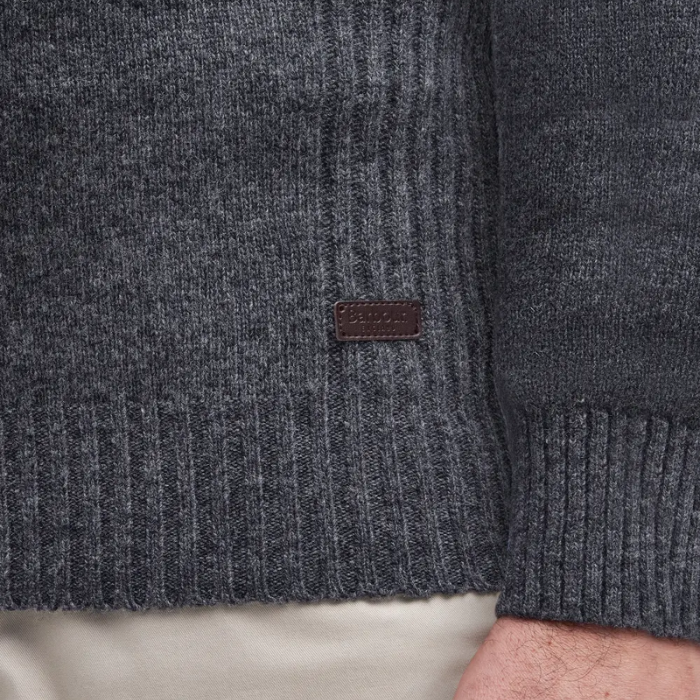 Close-up of a dark grey knitted jumper with a brand label on a neutral background