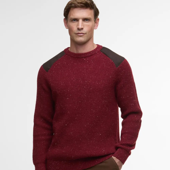 Man wearing a red Barbour jumper with dark shoulder panels on a light gray background