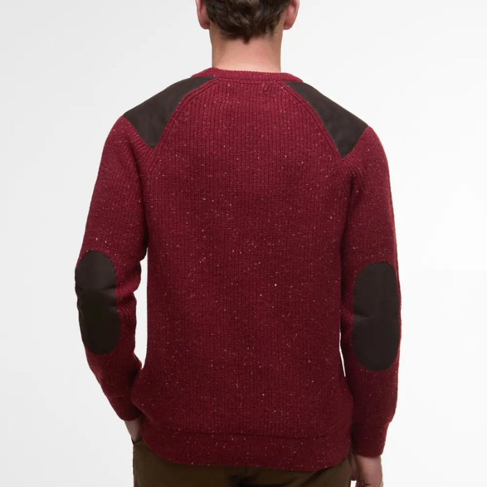 Red Barbour jumper with dark elbow patches worn by a person on a white background
