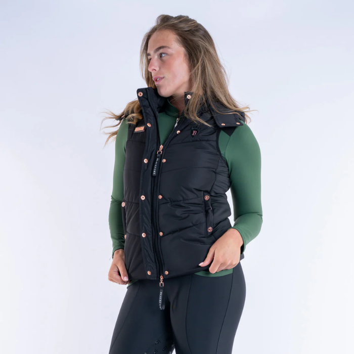 Woman wearing a black puffer gilet over a green base layer on a white background