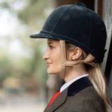 Woman wearing a black riding helmet with a beige face guard, outdoors.