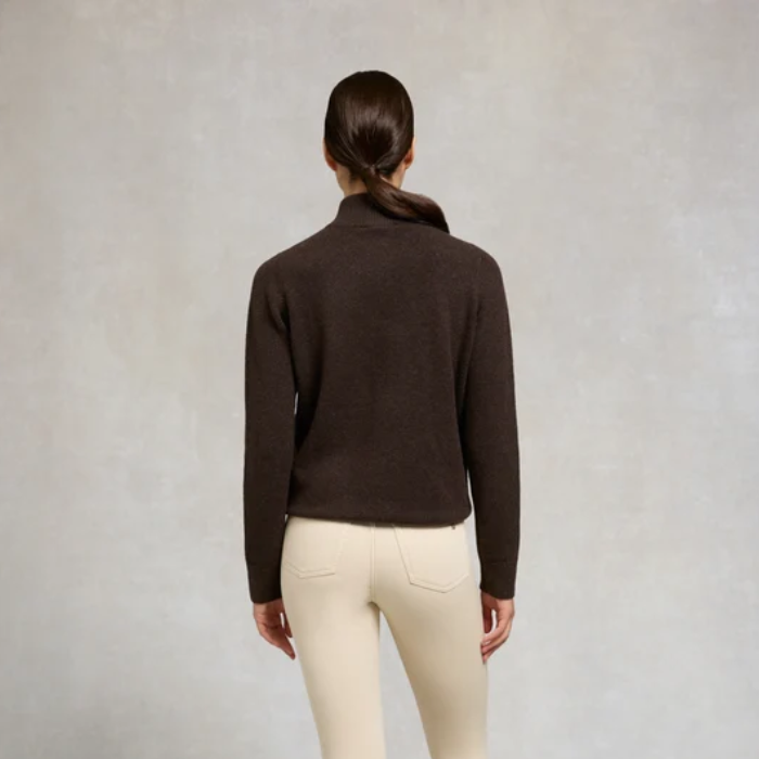 Holland Cooper Country Quarter Zip Knit Variant Colour Chocolate.
A woman viewed from behind wearing a dark brown cropped mock-neck knit sweater and cream-colored pants, standing against a textured light gray studio background.