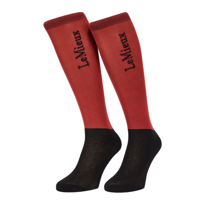 LeMieux AW26 Competition Socks 2 pack Variant Colour Russet.
A pair of knee-high socks with a russet red upper leg section and black feet, featuring the brand name 'LeMieux' printed in black script on the front of each sock, shown against a plain white background.