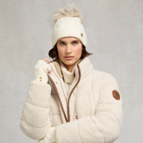 Lady wearing a cream bobble hat with a cream jacket against a grey background. 