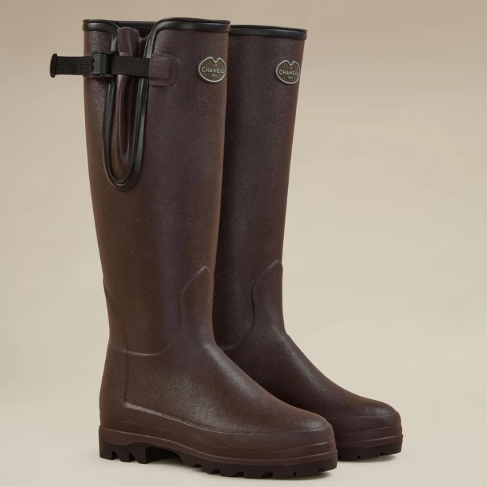 Le Chameau Ladies Vierzonord Neoprene Lined Wellies Variant Morron fonce/Black. A pair of dark brown rubber rain boots with black straps and buckles on the sides, displayed against a solid beige background.