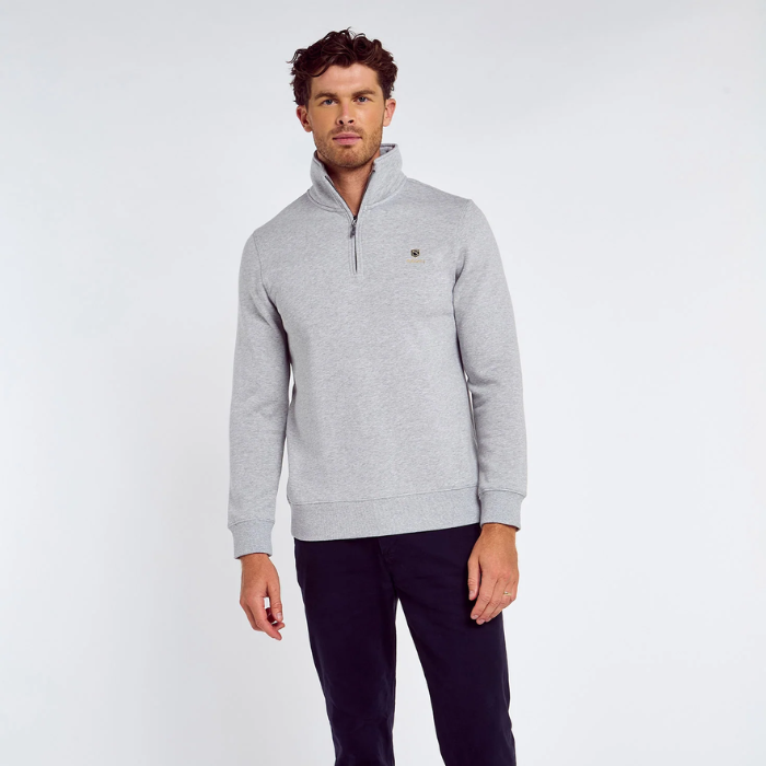 Man wears a grey zipped sweatshirt and dark jeans against a light grey background