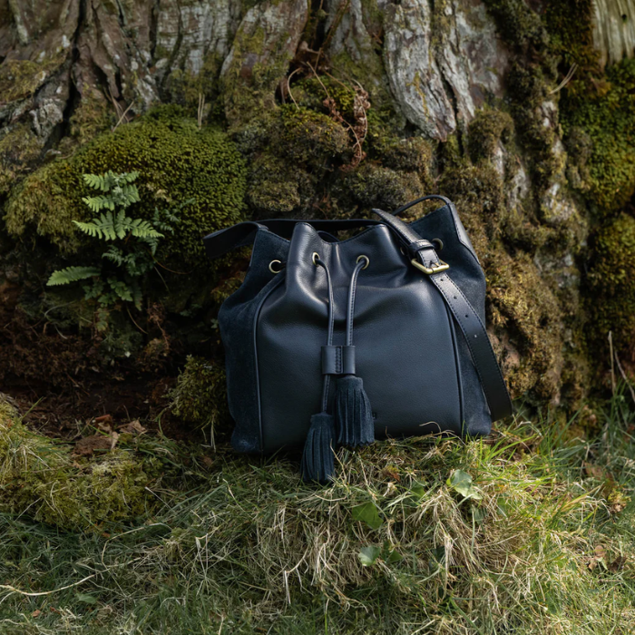 navy pouch style bag with black tassels with a tree in the background