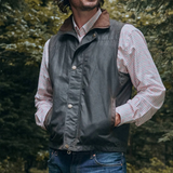 Man wearing a dark gilet over a plaid shirt with a forest background