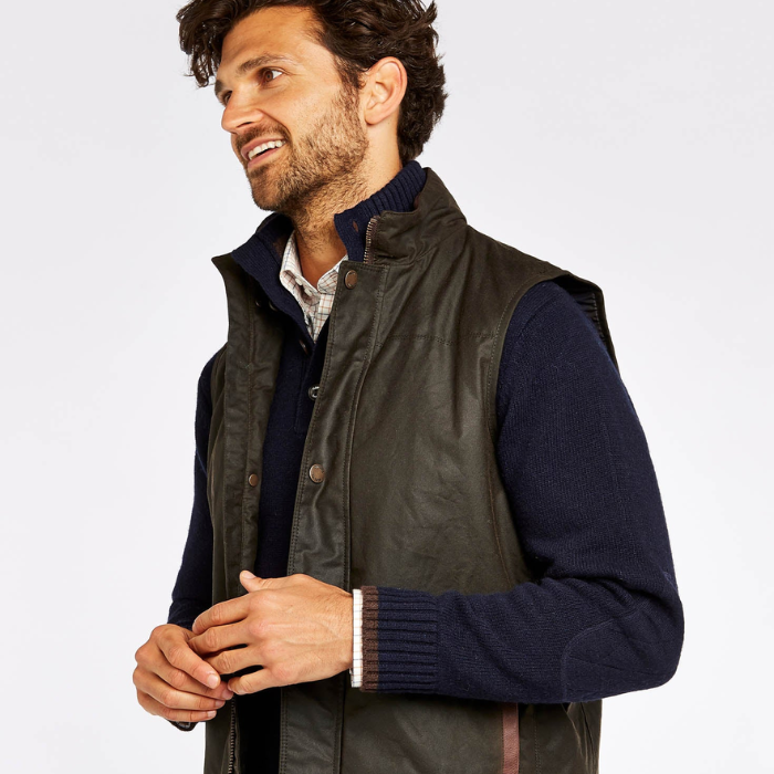 Man wearing a dark green gilet over a navy sweater on a light grey background