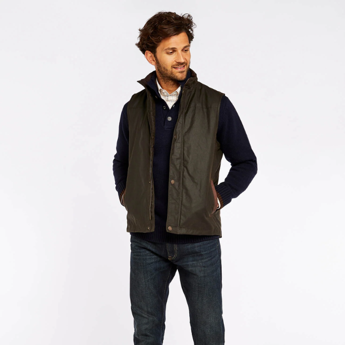 Man wearing a dark green gilet over a navy knit and jeans on a white background