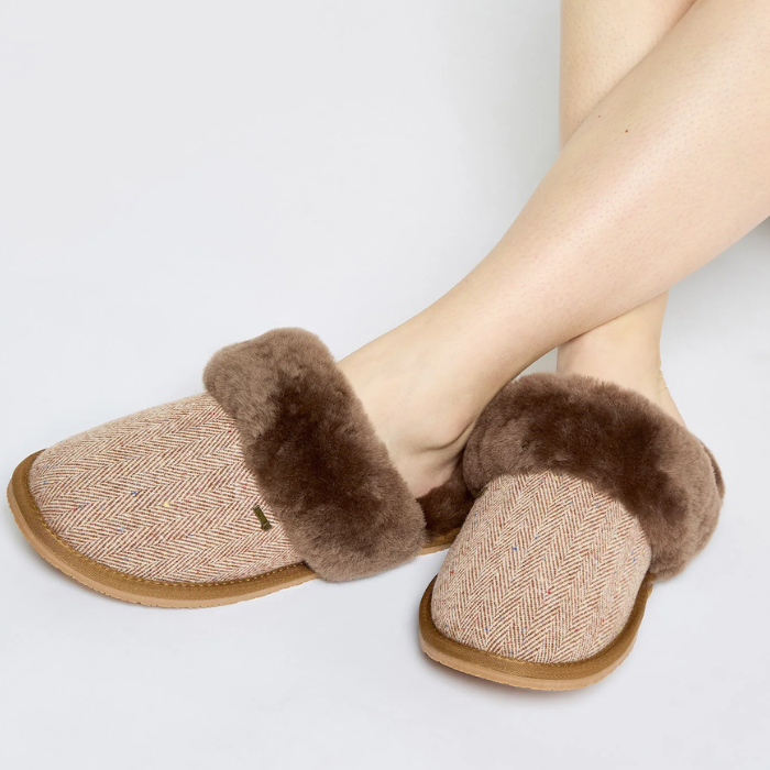 Pair of brown slippers with fuzzy trim worn by a person on a light grey background