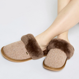 Pair of brown slippers with fuzzy trim worn by a person on a light grey background