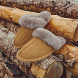 Pair of tan slippers with grey fur trim on a wooden log