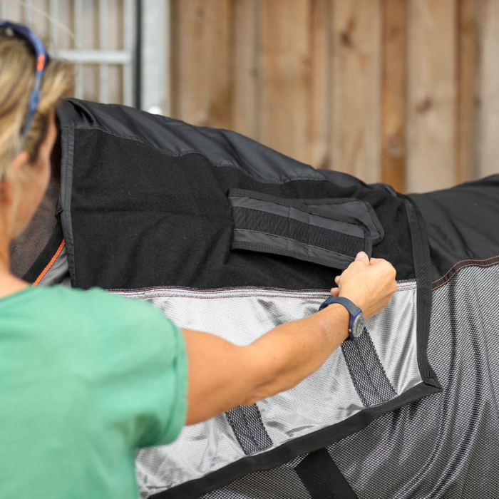 Person adjusting a black and grey horse rug on a horse.