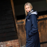 Person wearing a navy blue raincoat with a brand logo in front of a rustic wooden door.