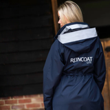 Person wearing a navy raincoat with 'REINCOAT LITE' branding, standing against a dark brick wall.