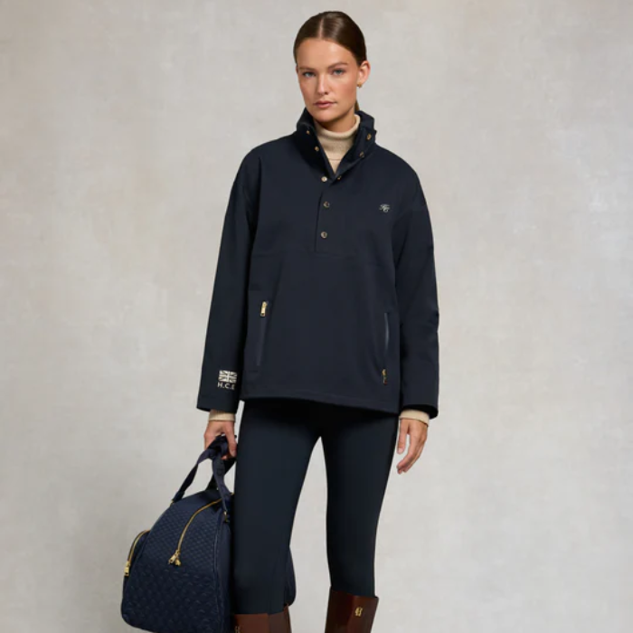 Woman wearing a navy blue jacket and holding a matching bag against a neutral background