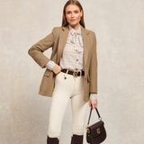 Woman wearing a brown blazer, white shirt, and white jeans, holding a leather handbag on a beige background