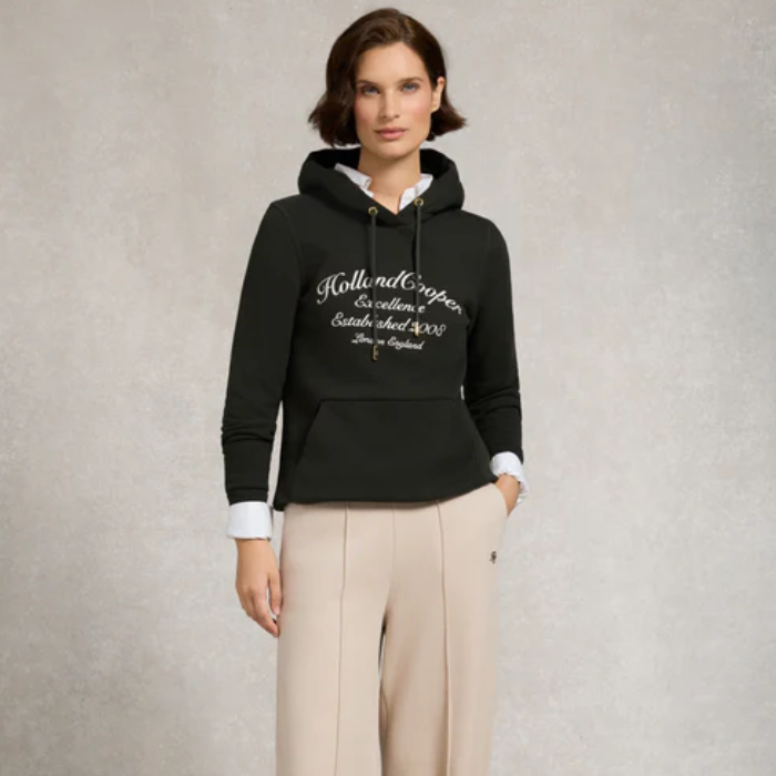Woman wearing a dark green hoodie with 'Holland Cooper' logo on a neutral background