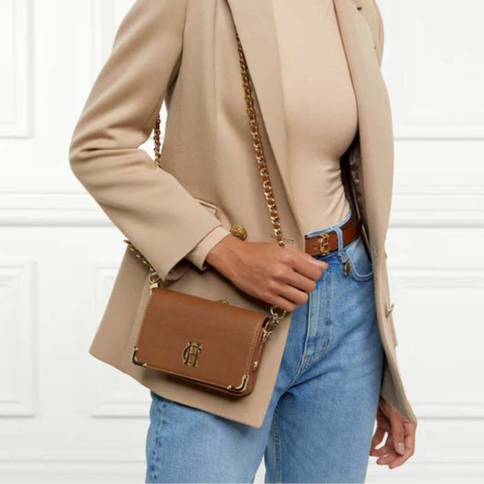 Person wears a brown leather handbag over their shoulder with a chain strap on white background
