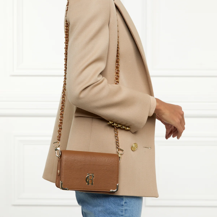 Person wearing a beige coat with a brown handbag against a white background