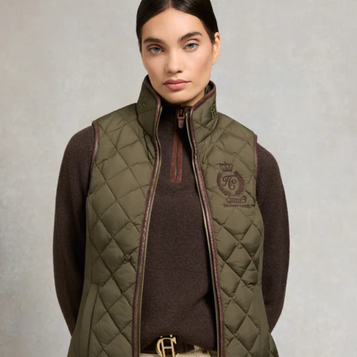 Woman wearing a green quilted gilet with a brand logo on a neutral background