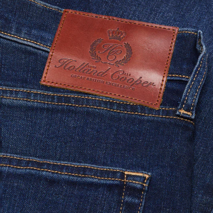 Close-up of a blue denim fabric with a brown leather label featuring 'Holland Cooper' branding.
