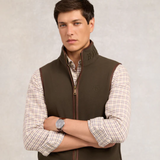 Man wearing a khaki vest over a plaid shirt with a neutral background