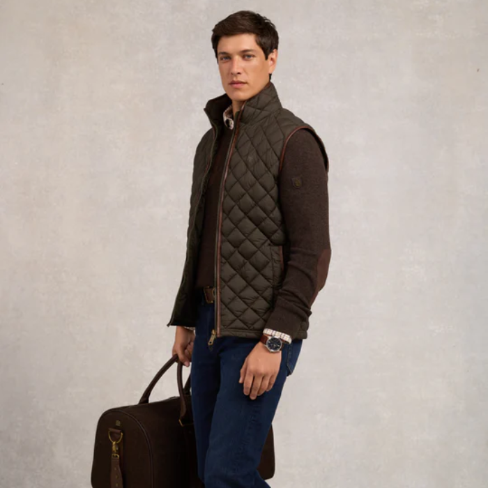 Man wearing a quilted gilet holding a leather bag against a neutral background