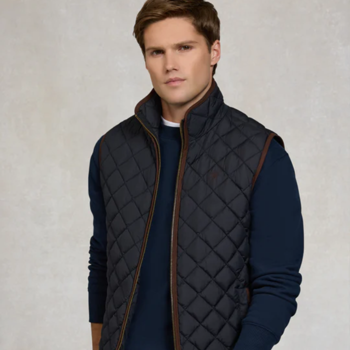 Man wearing a dark quilted gilet over a navy sweater on a light background