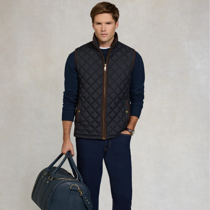 Man wearing a quilted gilet holding a duffel bag against a neutral background