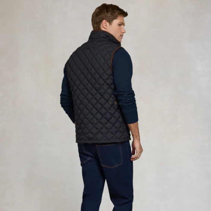 Man wearing a quilted navy gilet over a navy sweater and jeans on a light grey background